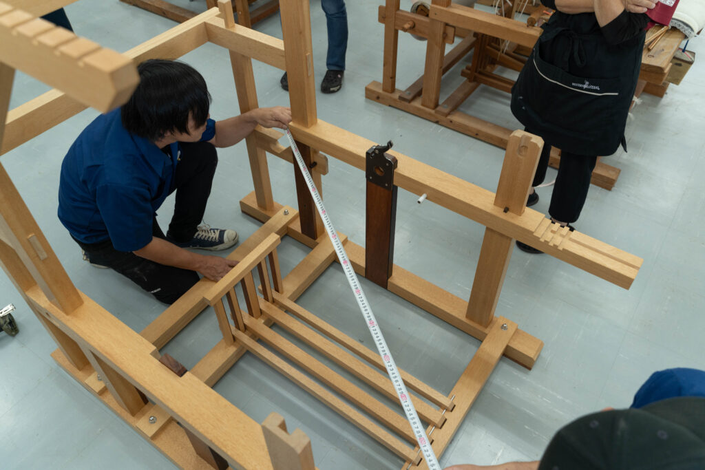 改良型織り機の寸法をメジャーで採寸し微調整する作業