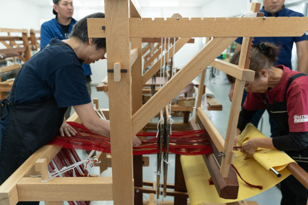 改良型織り機で試し織り中 赤いミンサー織りが織り上がっていく